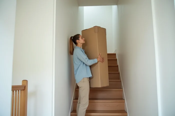 Femme testant si un grand meuble en carton peut passer dans la cage d'escalier d'une maison de style scandinave